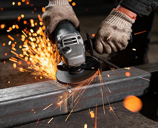 Ein Arbeiter bearbeitet mit einer Winkelschleifer Metall, wobei Funken in alle Richtungen sprühen.