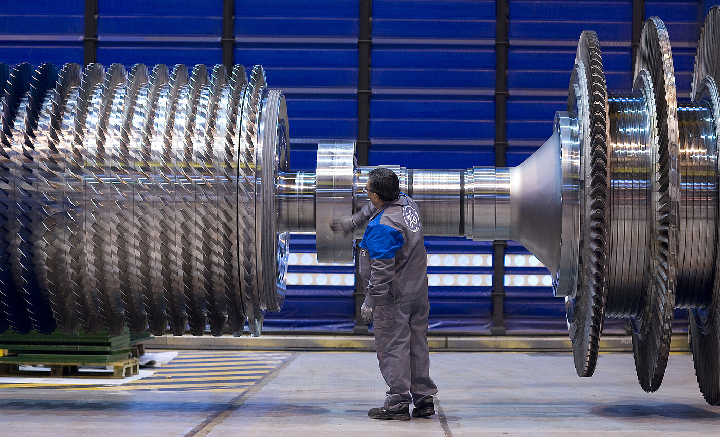 Ein Techniker überprüft präzise große Industriegetriebe oder Turbinenkomponenten in einer Fabrikhalle.