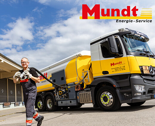 Ein Mitarbeiter von Mundt Energie-Service steht lächelnd neben einem gelben Tankfahrzeug auf einem Firmengelände.
