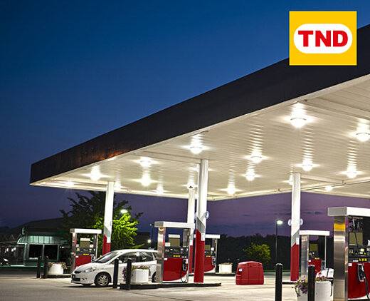 Beleuchtete Tankstelle bei Abenddämmerung mit mehreren Zapfsäulen und dem Logo von TND